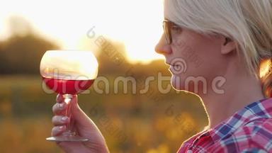 一个女人正在<strong>品尝红酒</strong>。 日落时分，站在葡萄园旁边的酒杯